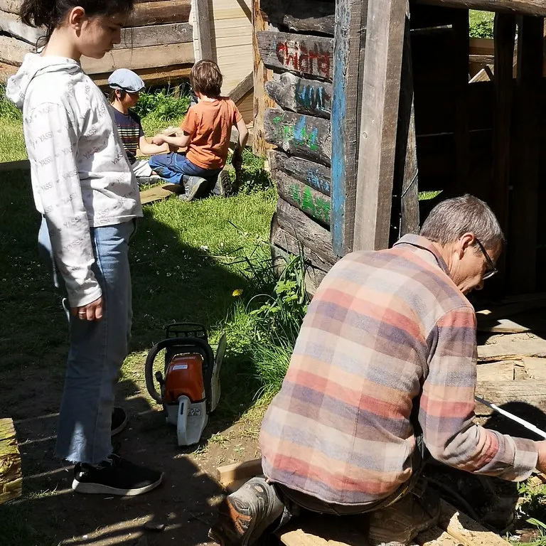 Kinder und ein Erwachsener bauen an einer Holzhütte.